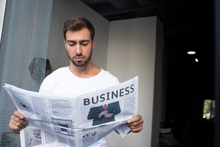young man in white t-shirt reading a business newspaper
